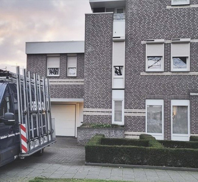 Zicht op een woning met elektrische rolluiken en garage, omgeven door een nette tuin in Limburg.