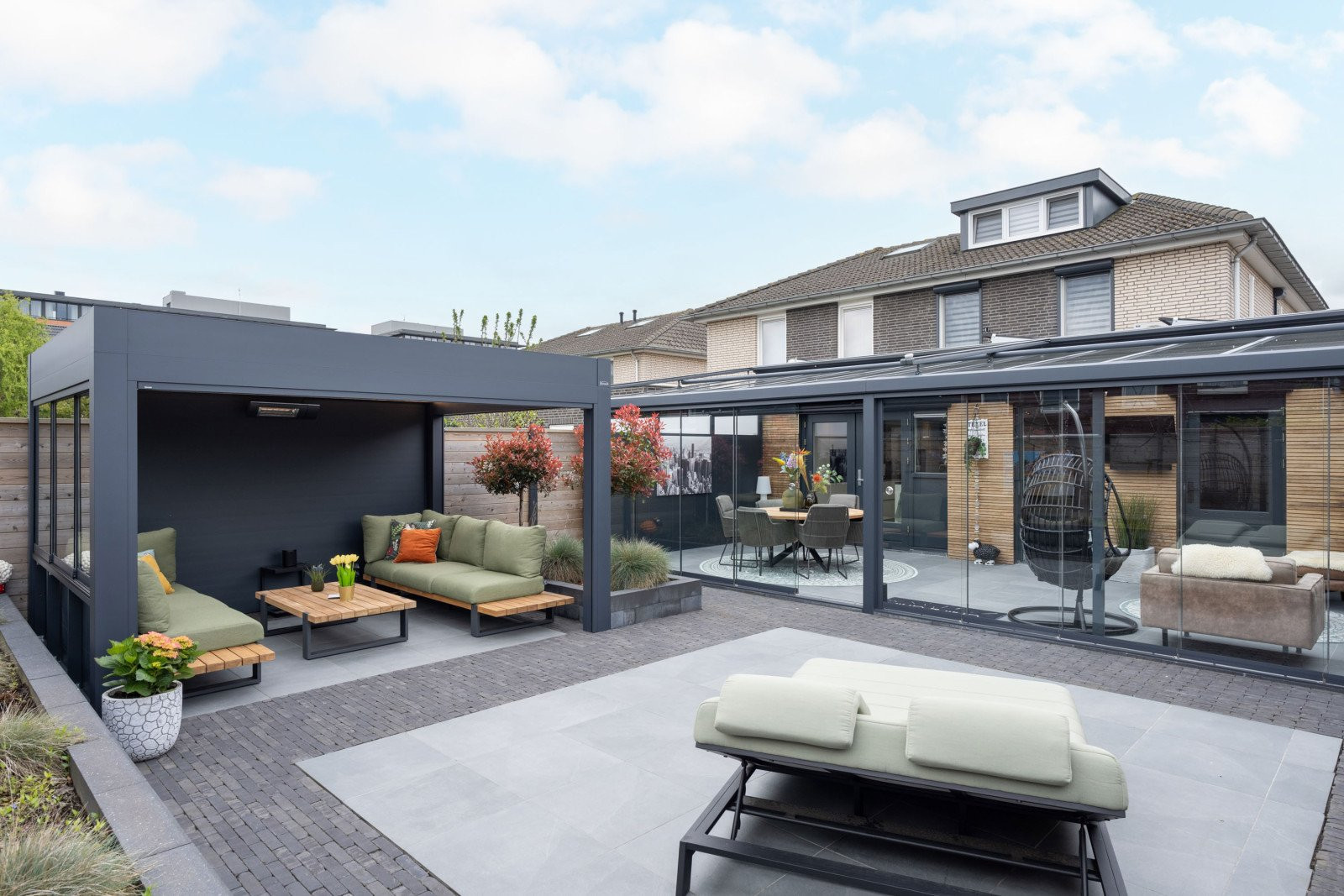 Vrijstaande terrasoverkapping met comfortabele zithoek en groene kussens in een strakke onderhoudsarme tuin.