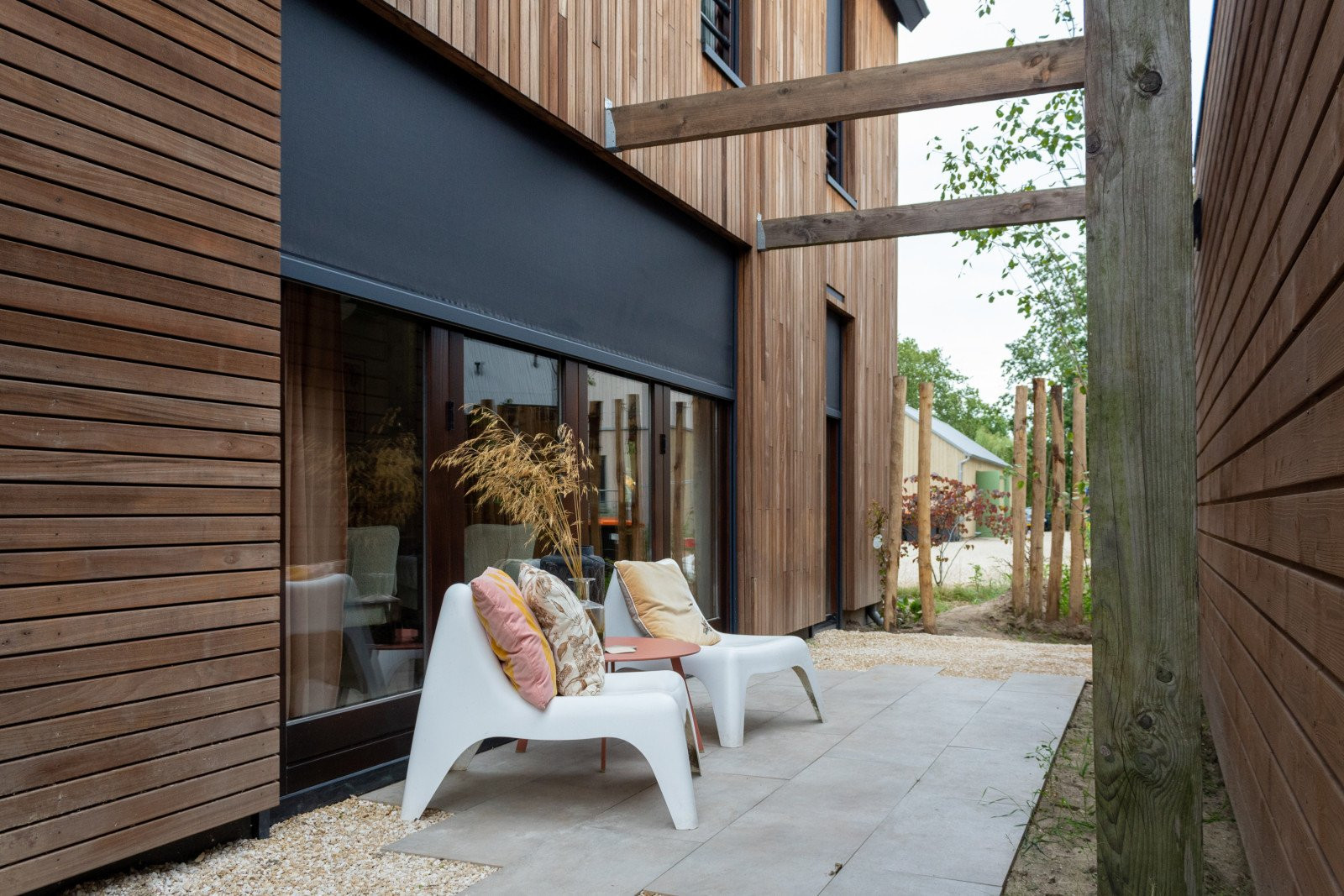 Luxe ritzscreen voor zonwering naast design terrasmeubels op tuinterras.
