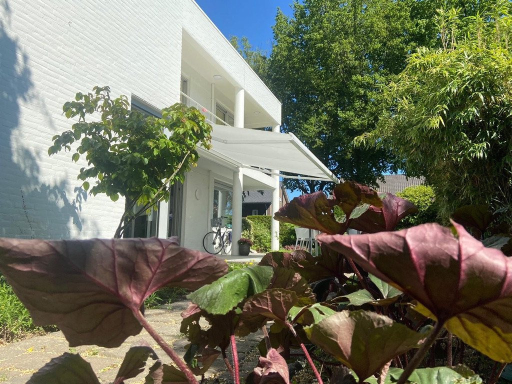 Knikarm zonnescherm aan een moderne woning, zonwering biedt schaduw en bescherming tegen de zon in de tuin.