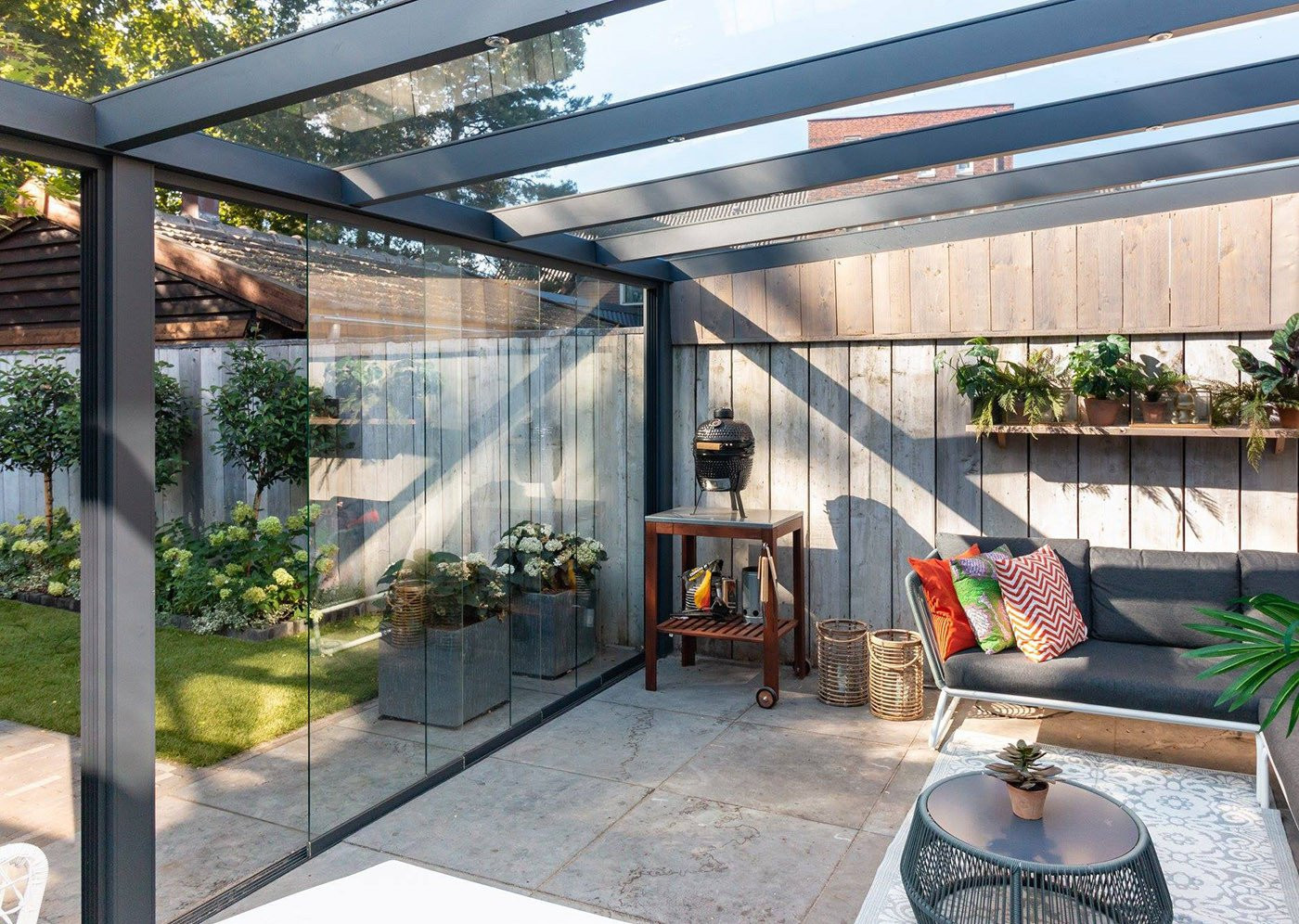 Vrijstaande terrasoverkapping met glazen schuifwanden en een stijlvol ingericht interieur.