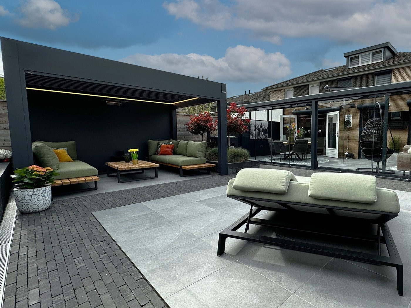 Vrijstaande overkapping met zithoek en groene lounge set in moderne tuin.