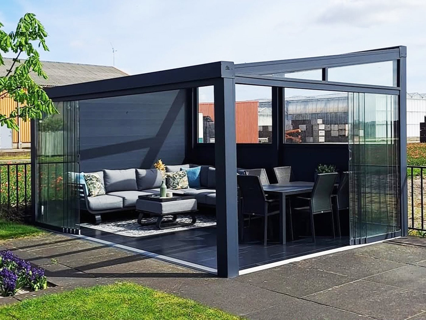 Vrijstaande terrasoverkapping met glazen schuifwanden en comfortabele tuinmeubelen, ideaal voor buitenontspanning.