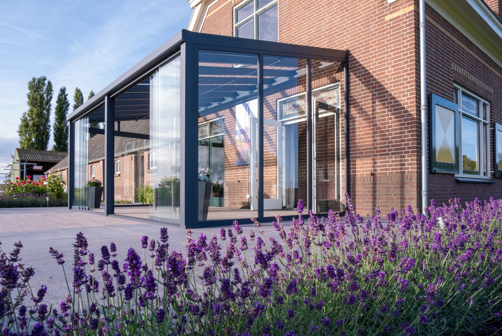 Terrasoverkapping met glazen schuifwanden, biedt beschutting en sfeer, omringd door lavendel in de tuin.