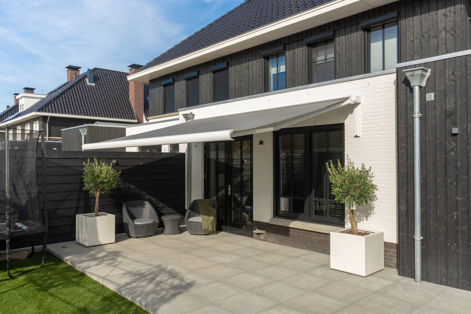 Grijs knikarmscherm biedt schaduw aan uw woning met als resultaat een koele woning.