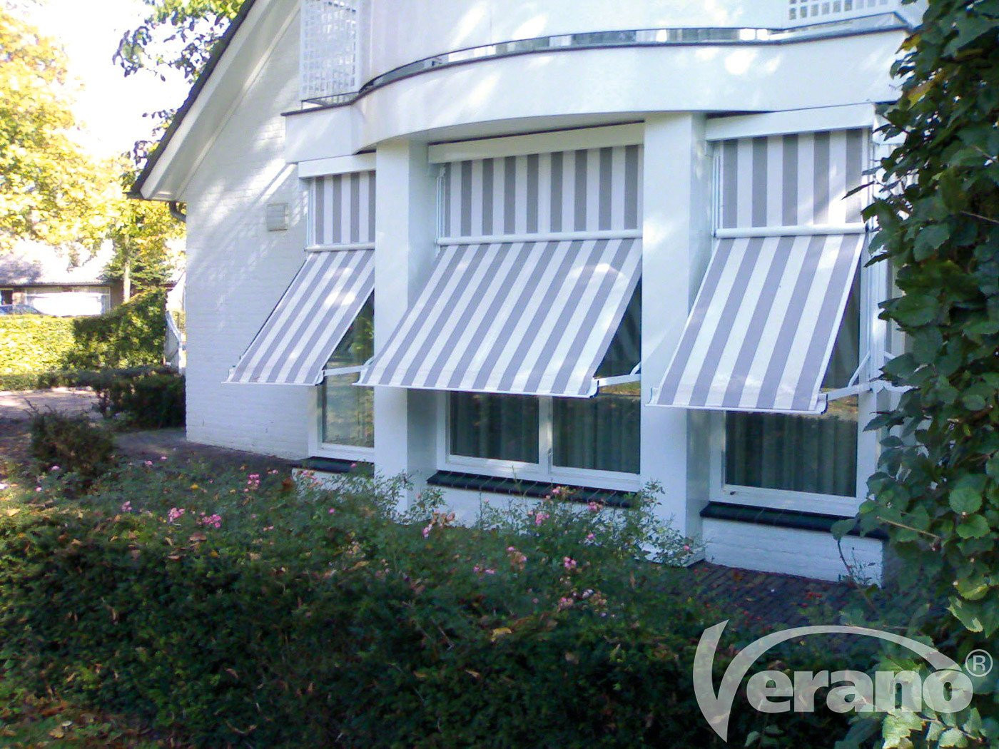 Strakke uitvalschermen wit grijs gestreept, gemonteerd aan een woning voor zonwering en privacy.