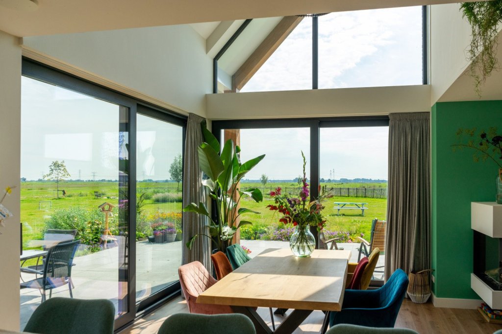 Kozijnen in Sittard - Geleen of elders in Limburg. Eetkamer met luxe kozijnen en uitzicht op de tuin, ingericht met een houten tafel en kleurrijke stoelen.