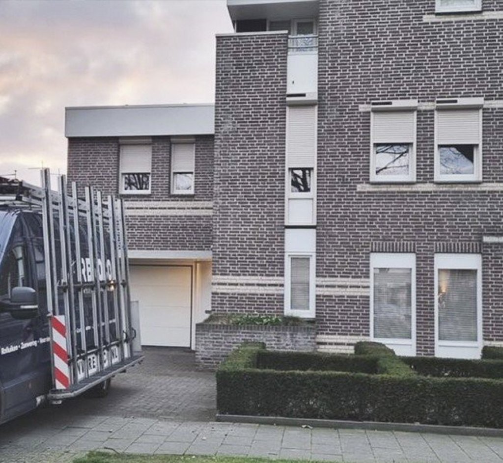 Zicht op een woning met elektrische rolluiken en garage, omgeven door een nette tuin in Limburg.