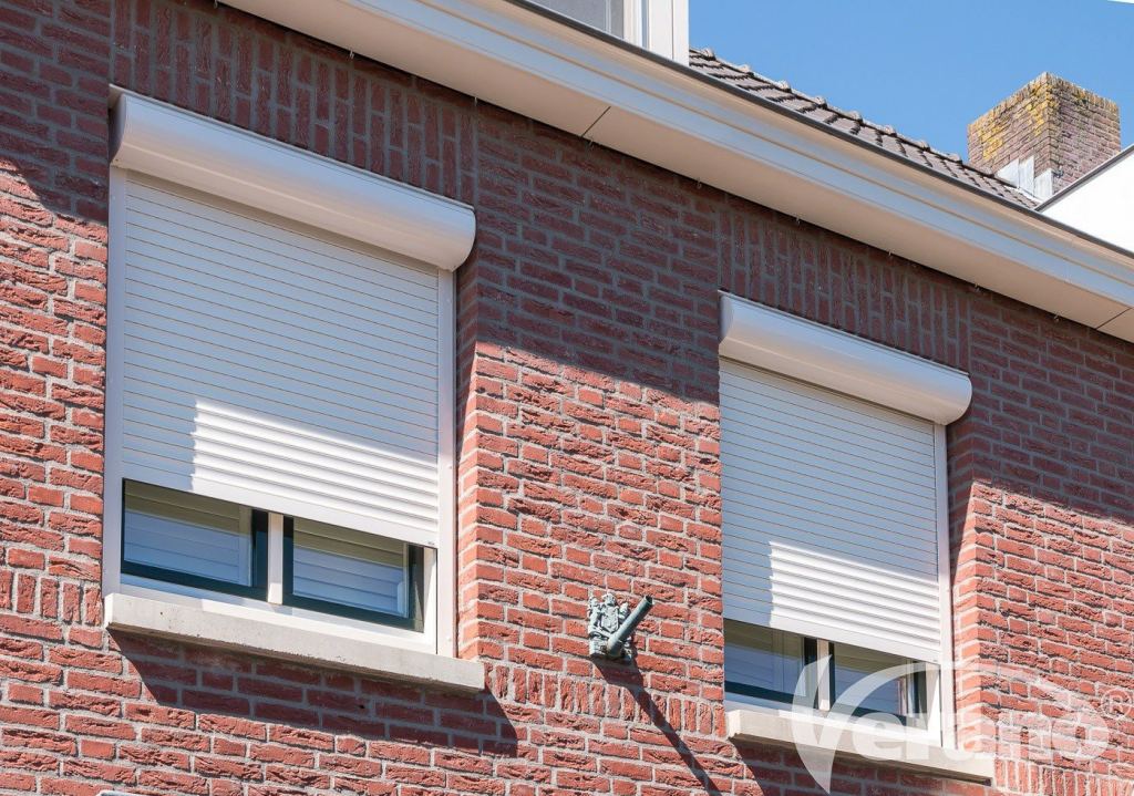 Manually operated roller shutters in a light colour, fitted to a brick fa&ccedil;ade, ideal for privacy and sun shading.