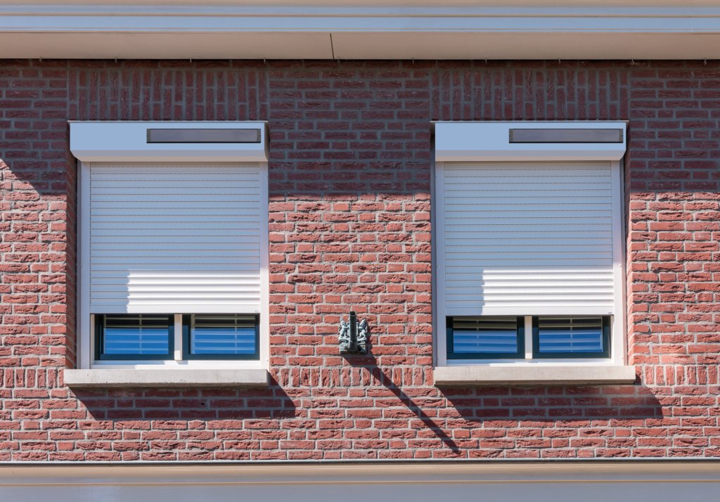 Ontdek stijlvolle solar rolluiken voor uw woning!. Strakke witte solar rolluiken op een modern bakstenen huis met blauwe raamkozijnen.