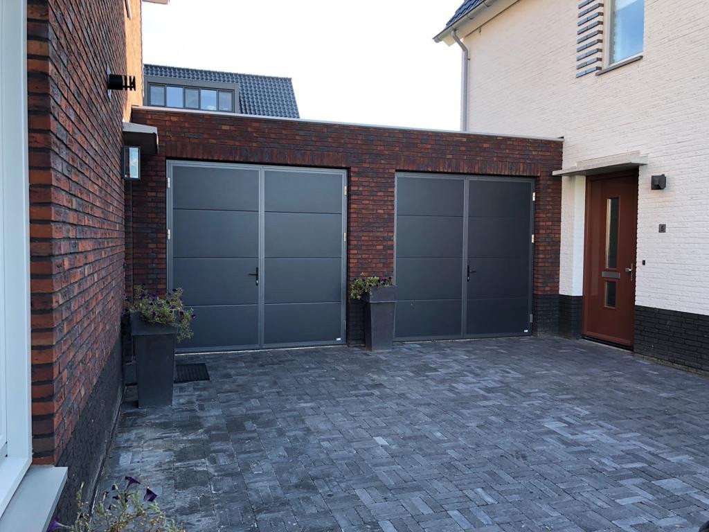 Stijlvolle openslaande garagepoorten voor jouw woning. Moderne grijze openslaande garagepoorten, stijlvol geïntegreerd in een brick wanden met een nette oprit.