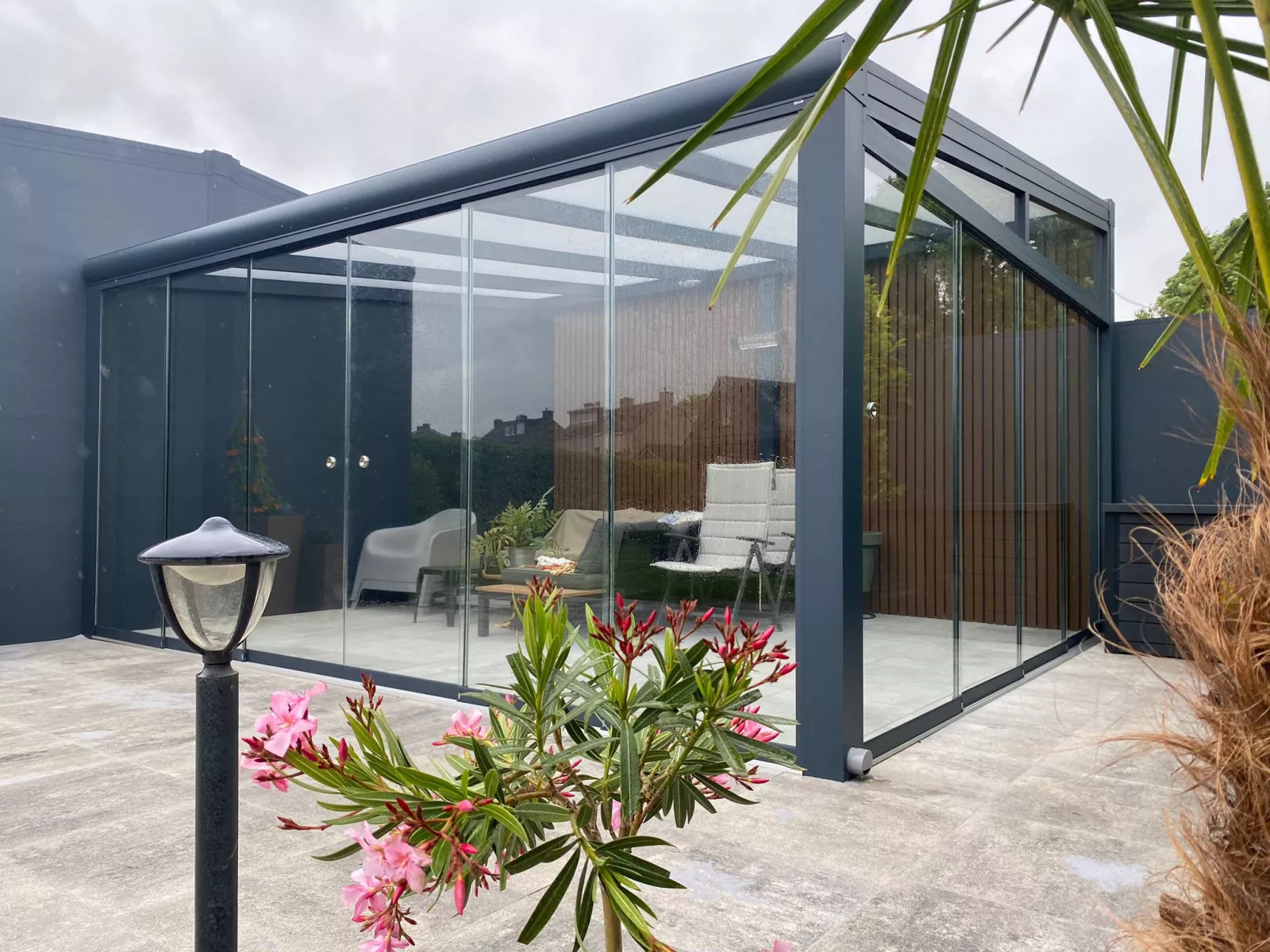 Aluminium-Terrassenüberdachung mit Glasschiebewänden und WPC-Wandverkleidung in einem modernen Garten