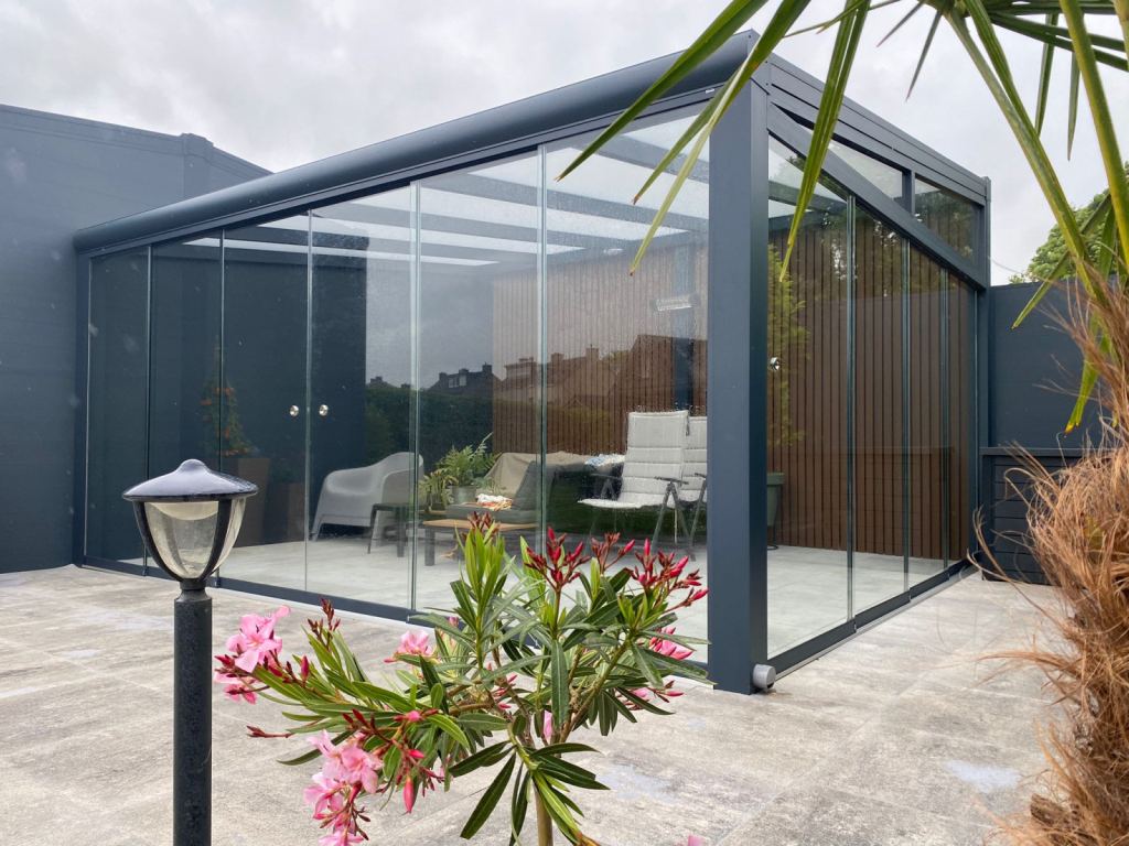 Aluminium-Terrassen&uuml;berdachung mit Glasschiebew&auml;nden und WPC-Wandverkleidung in einem modernen Garten.