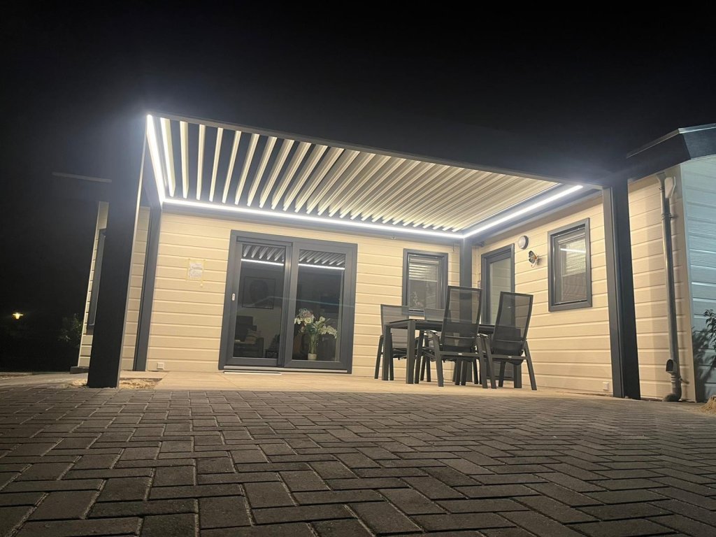 Moderne terrasoverkapping met lamellendak en sfeervolle verlichting, perfect voor buiten dineren.