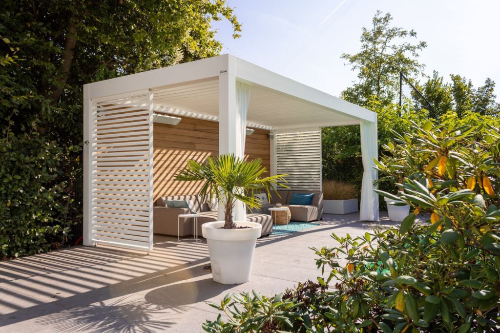 Freestanding patio cover with a louvred roof and shutter panels, ideal for regulating the sunlight and relaxing on your lounge set.