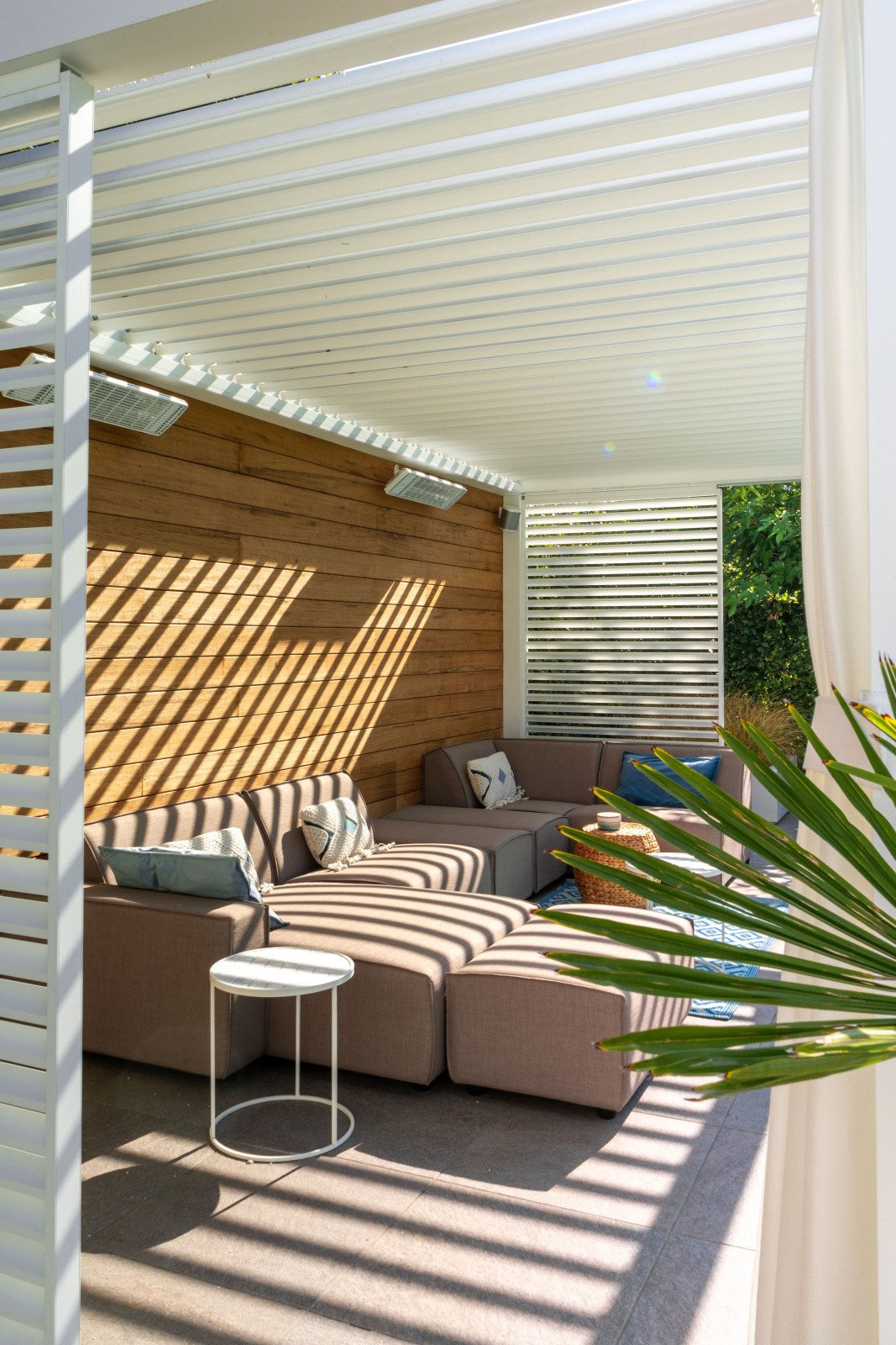 Heerlijk genieten van uw eigen overkapping met terrasverwarmers? Bezoek Renoco in Sittard! Sfeervolle loungehoek met loungebank onder een lamellendak met terrasverwarmers en moderne tuinmeubelen.