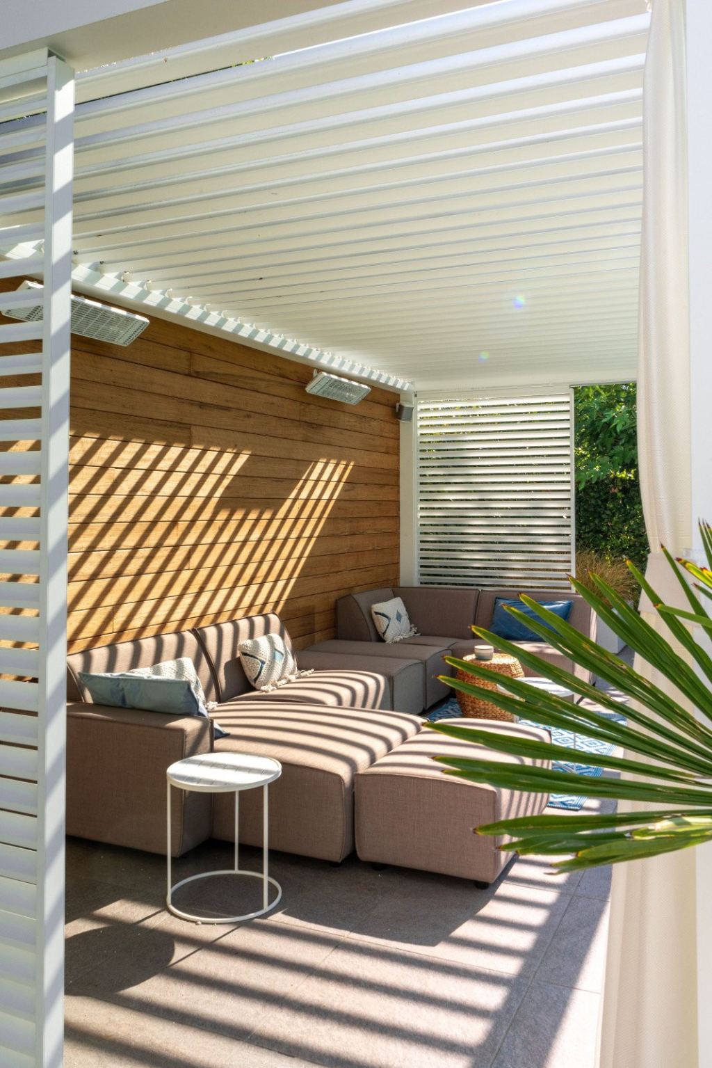Inviting lounge corner with a lounge sofa under a louvred roof, with patio heaters and modern garden furniture.