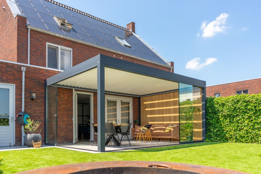 Elegante lamellendak terrasoverkapping voor uw tuin in Sittard. Modern lamellendak terrasoverkapping met glazen zijkanten en stijlvolle meubels in een tuin achter een huis.