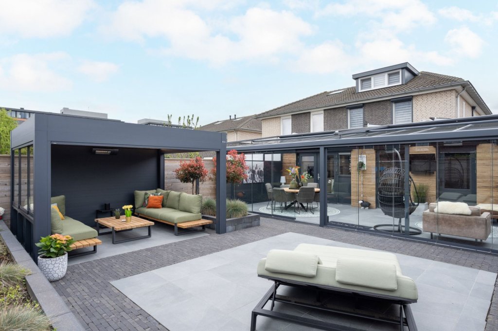 Vrijstaande overkapping voor uw tuin? Renoco plaatst in Sittard - Geleen en elders in Limburg. Vrijstaande terrasoverkapping met comfortabele zithoek en groene kussens in een strakke onderhoudsarme tuin.