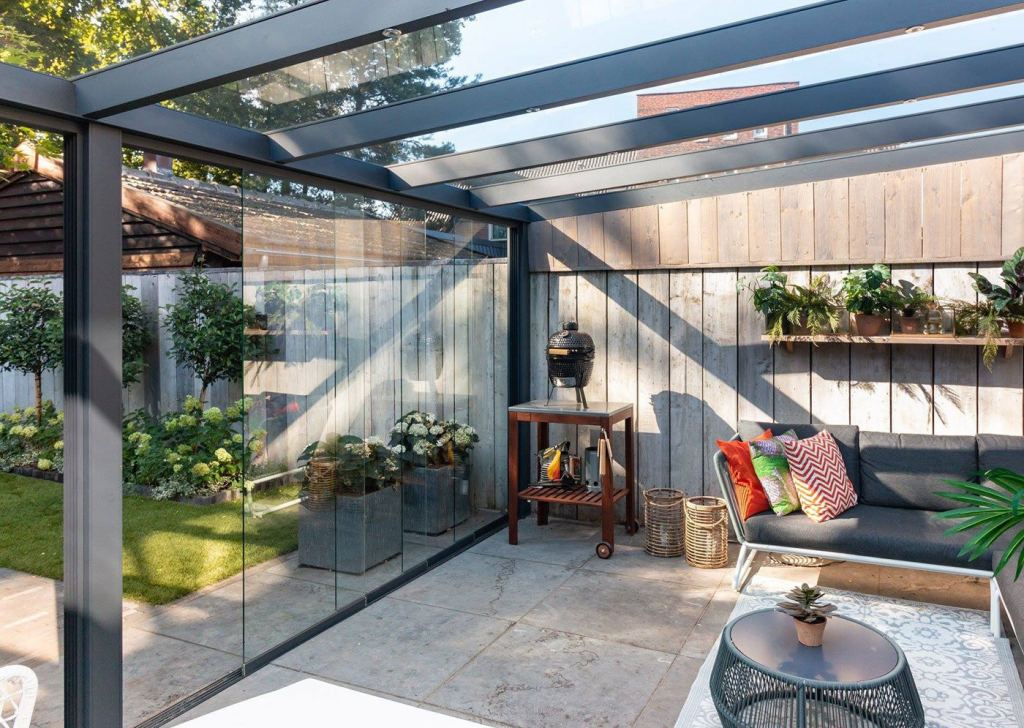 Moderne Terrassen&uuml;berdachung mit Glasw&auml;nden und einer stilvollen Sitzecke mit Grill.