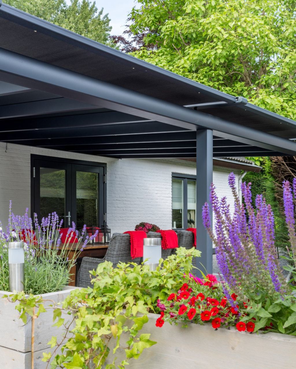 Moderne Veranda am Haus mit Terrassendach-Beschattung in einem gr&uuml;nen Garten mit vielen Blumen und einladenden Sitzgelegenheiten.