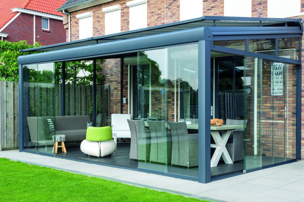 Stijlvolle glazen terrasoverkapping voor uw tuin!. Moderne glazen terrasoverkapping aan een huis met comfortabele meubels en een eettafel in Sittard.