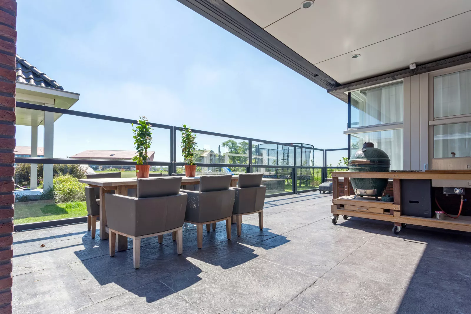 Modern glass windscreen on a patio with garden furniture, plants and an egg-style barbecue.