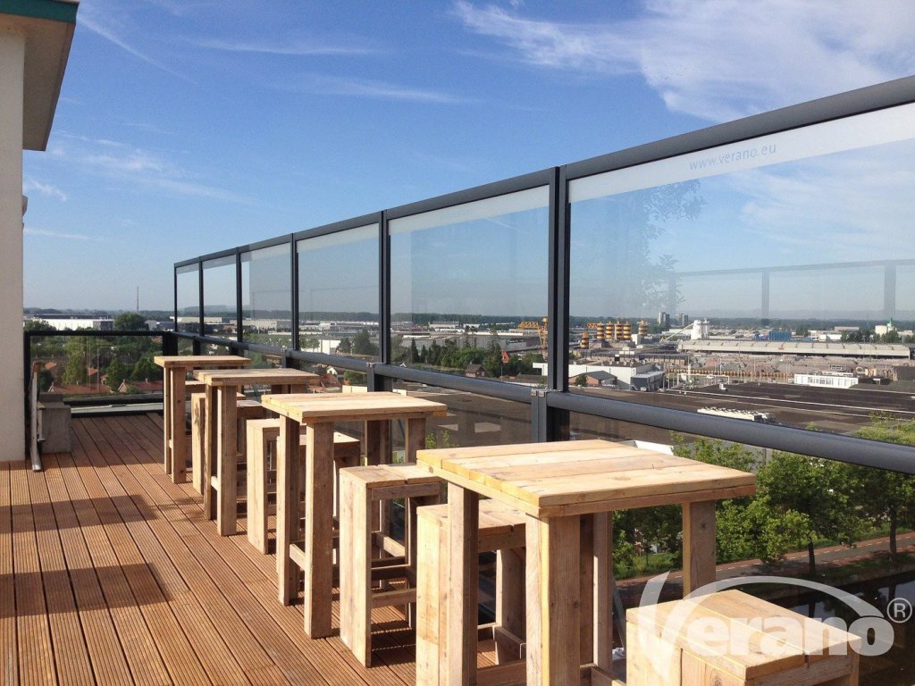 Glazen windschermen op dakterras met uitzicht over de stad met moderne houten tuinmeubelen.