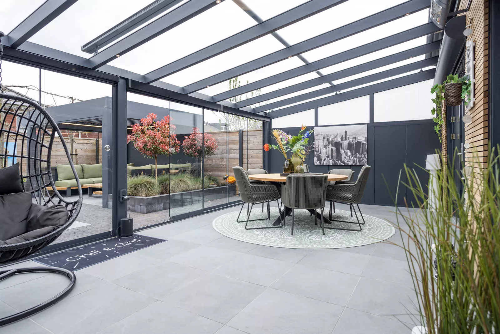 Luxuriöse Terrassenüberdachung aus Aluminium mit Glasschiebewänden, stimmungsvoller Einrichtung und viel Tageslicht. Ein komfortabler Außenbereich, um Ihren Garten das ganze Jahr über zu genießen.