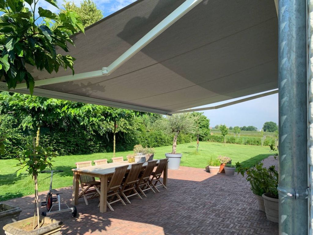 Knikarm zonnescherm biedt schaduw op het terras van een mooie groene tuin.