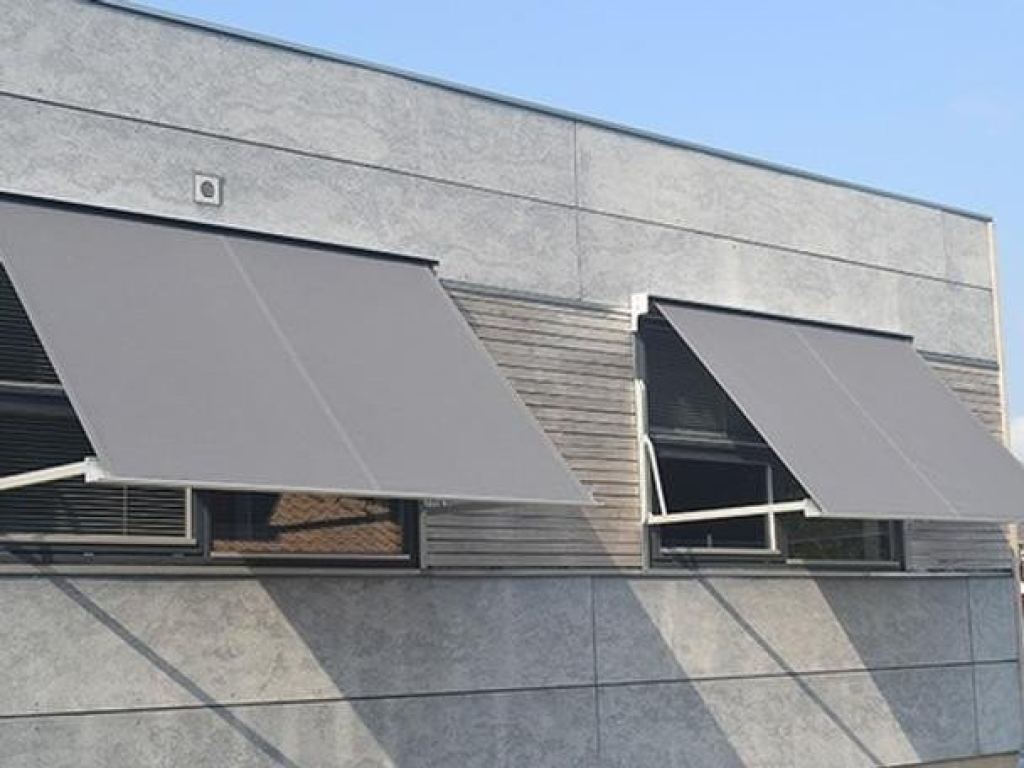 Grey drop-arm awnings installed on a modern fa&ccedil;ade, providing effective external sun shading for windows.