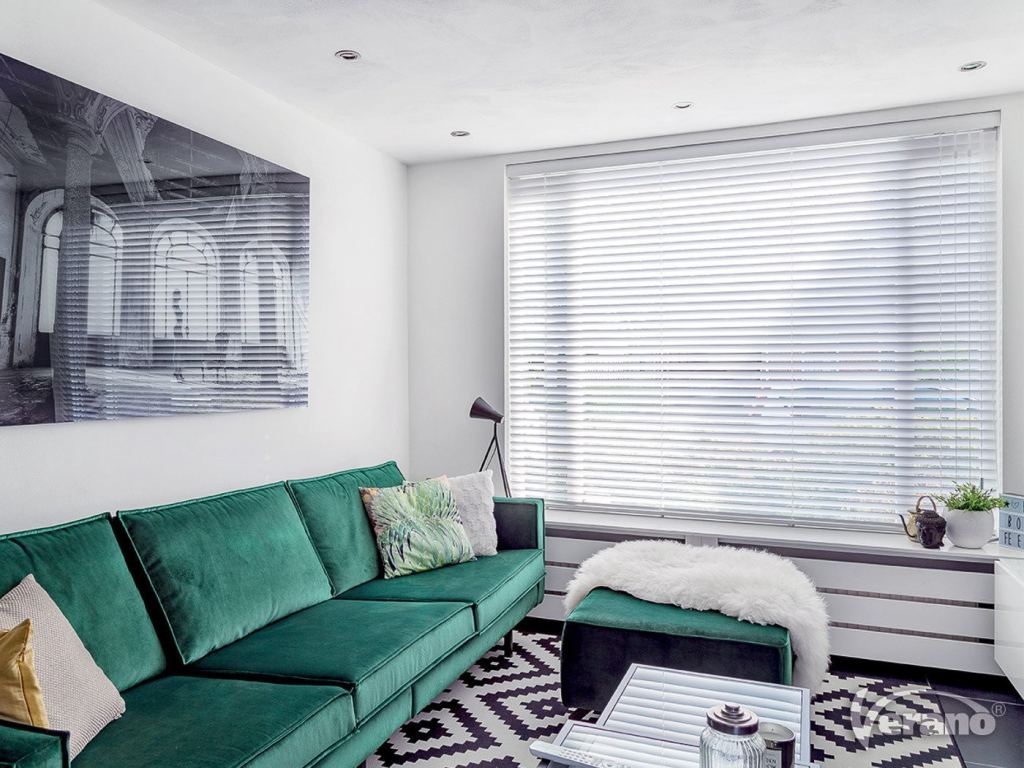 Jaloezie&euml;n op maat in een moderne woonkamer met groene bank en stijlvolle decoratie.