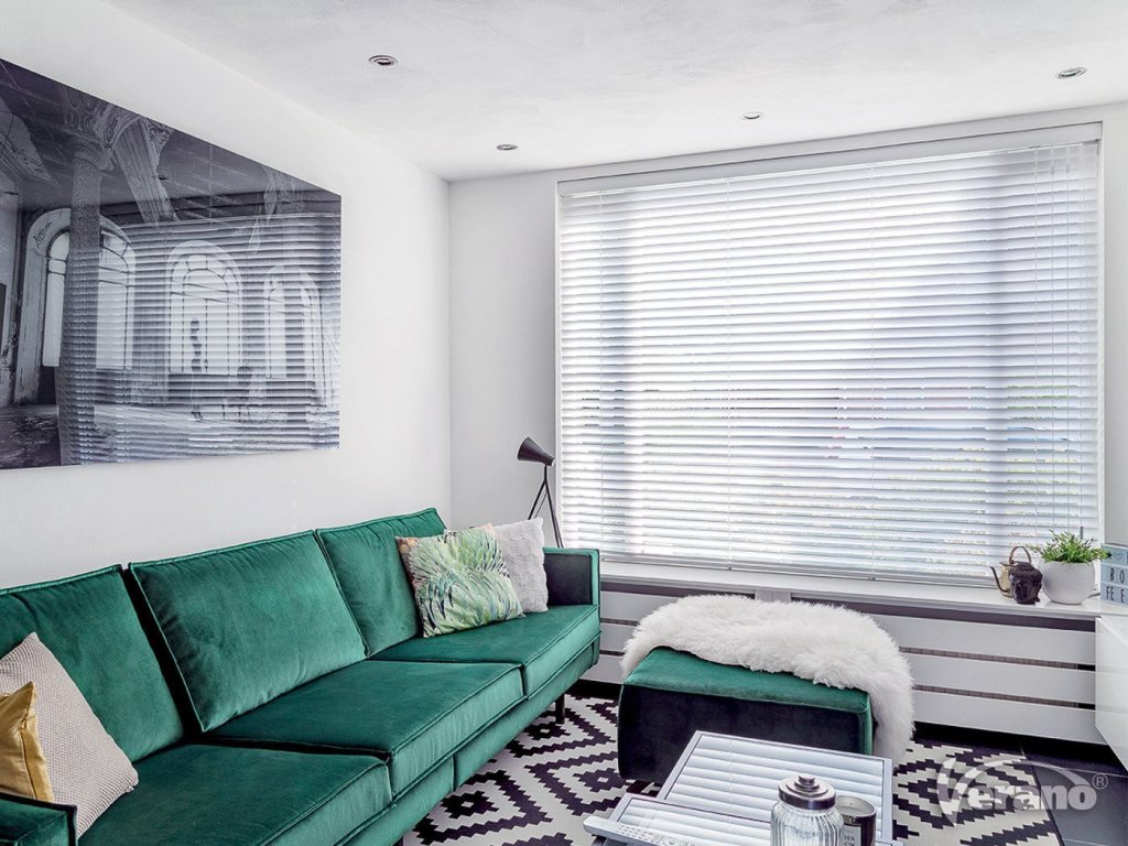 Jaloezie&euml;n op maat in een moderne woonkamer met groene bank en stijlvolle decoratie.