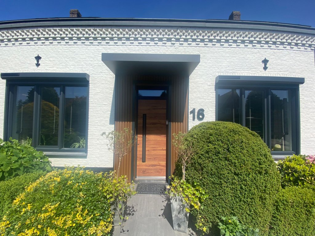 Moderne entree met houtlook voordeur en een groene zonnige voortuin.