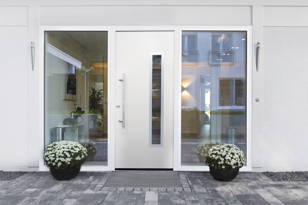 Strakke witte moderne voordeur met glazen panelen met zilveren handgreep, stoep aangekleed met bloempotten.