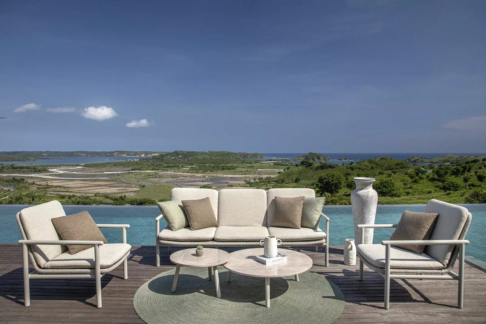 Moderne Gartenmöbel, zwei Sessel und ein Sofa mit Kissen, vor einer herrlichen Aussicht und einem Pool.