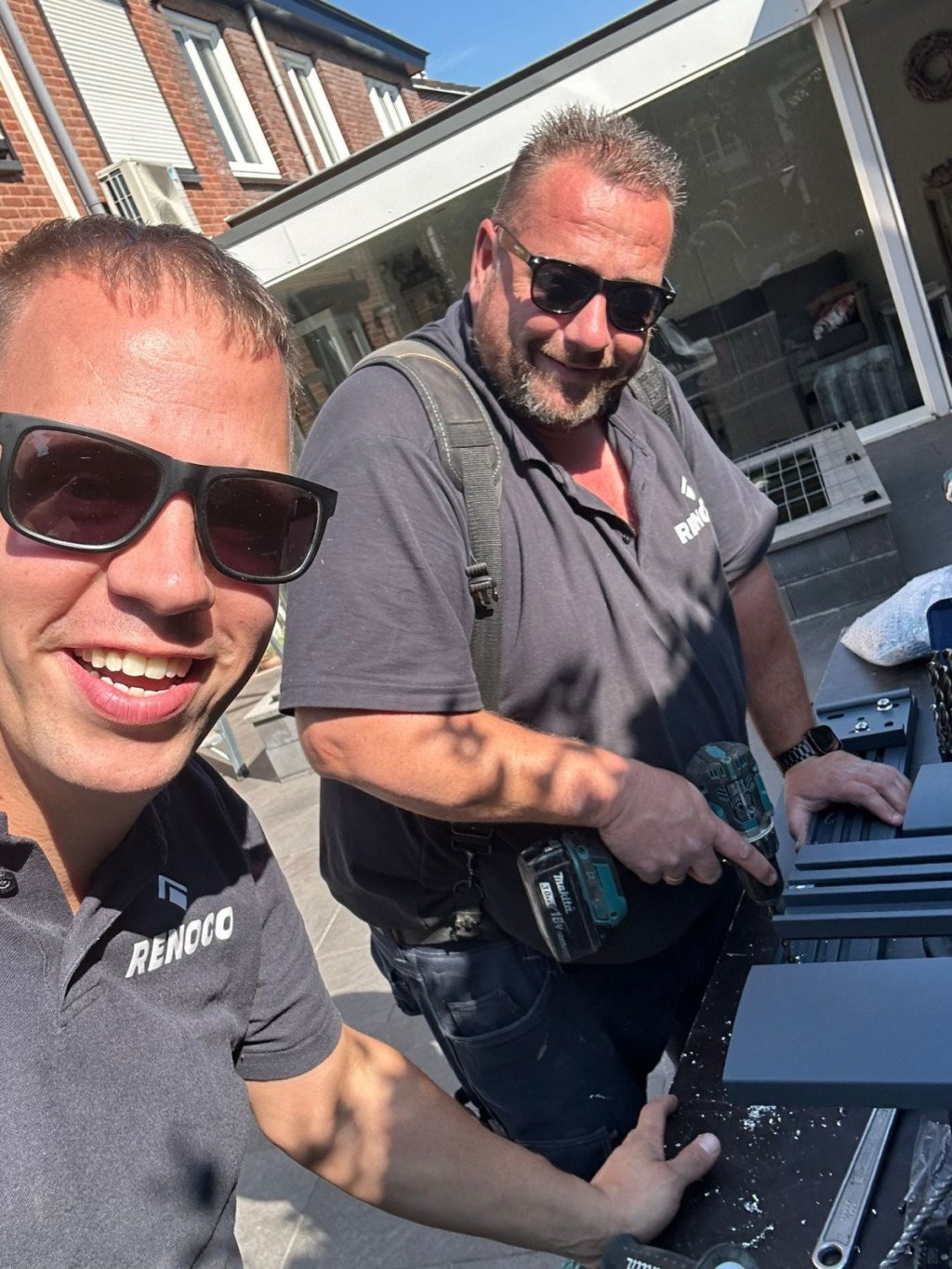 Professioneel team van Renoco in actie voor uw project!. Twee Renoco-medewerkers werken samen aan een product installatie met gereedschap in een tuinomgeving.
