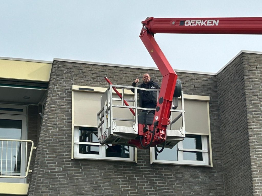 Servicemonteur van Renoco werkt vanuit een hoogwerker aan zonwering bij een woning

Title-tekst:.