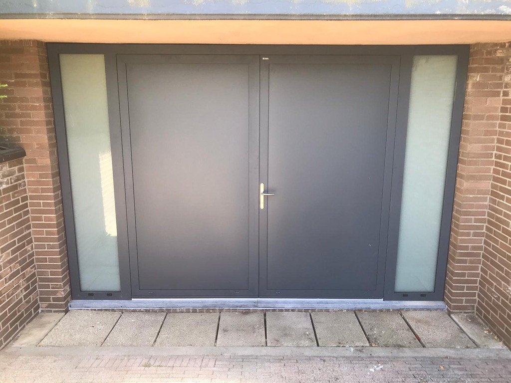 Dubbele garagedeur in Sittard-Geleen én Limburg. Grijze dubbele garagedeur met glaspanelen in Sittard-Geleen én Limburg.