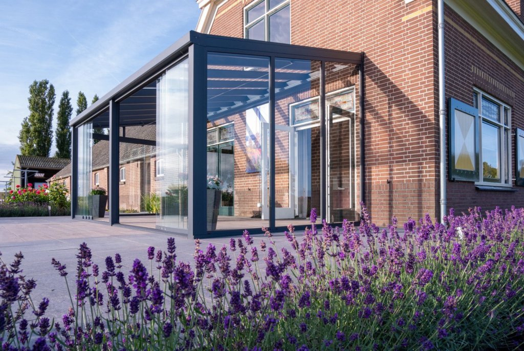 Terrasoverkapping met glazen schuifwanden. Terrasoverkapping met glazen schuifwanden, biedt beschutting en sfeer, omringd door lavendel in de tuin.