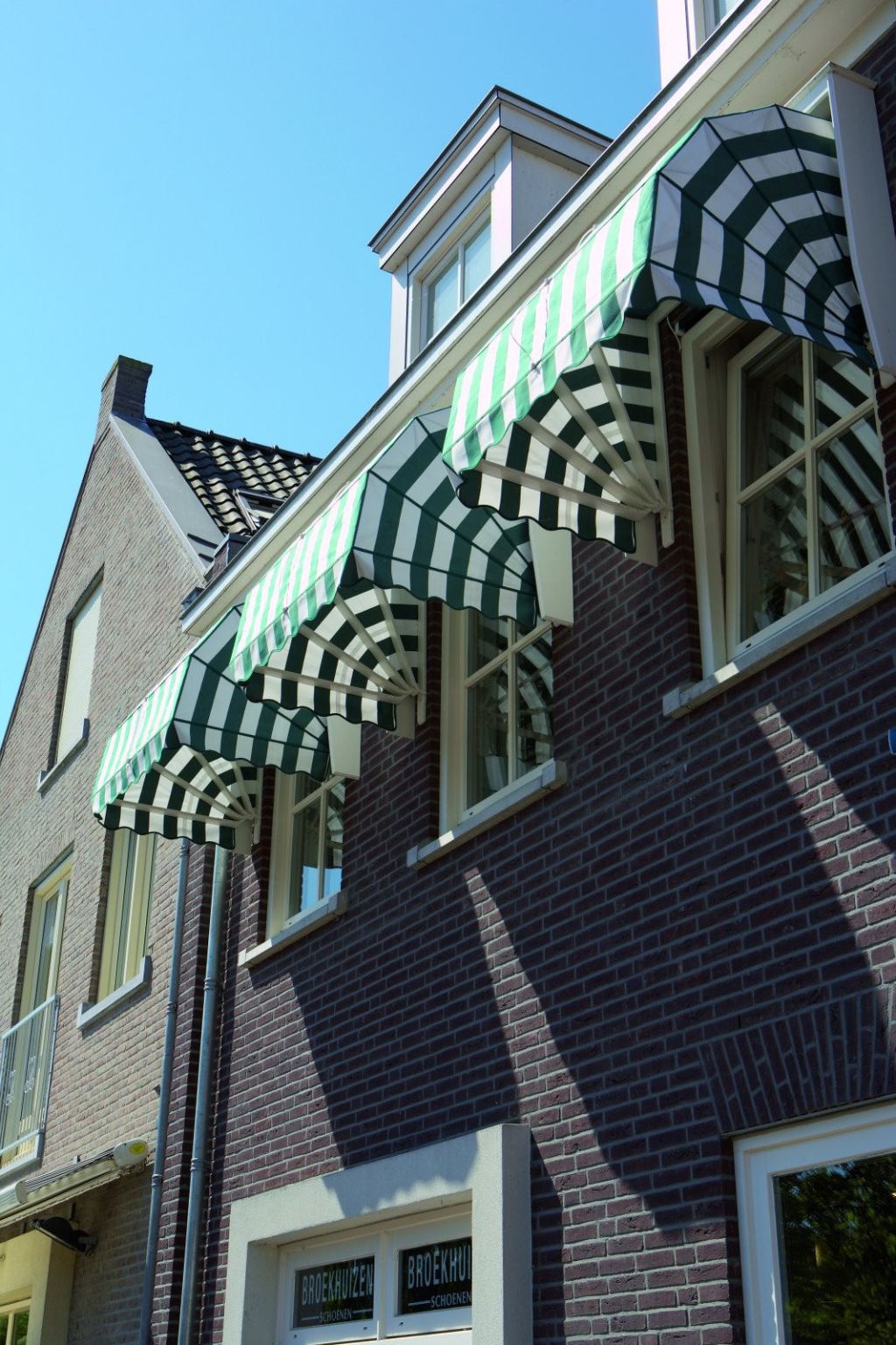 Elegant green-and-white striped Dutch canopies provide shade and privacy on the upper floor.