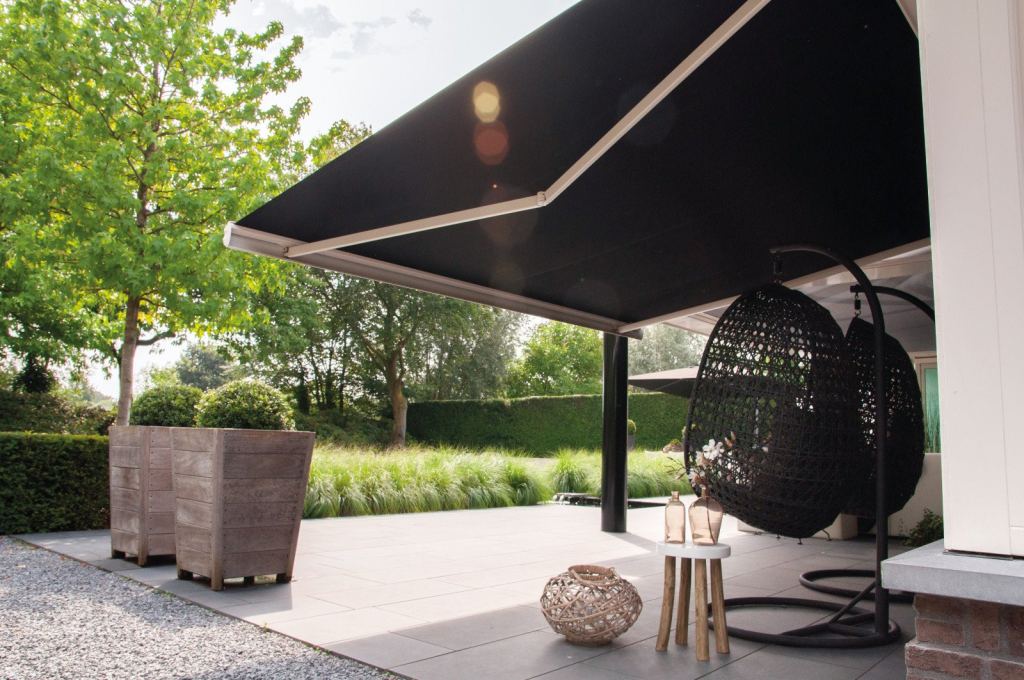 Elegant black folding-arm awning shading a stylish patio with a hanging chair and decorative touches.