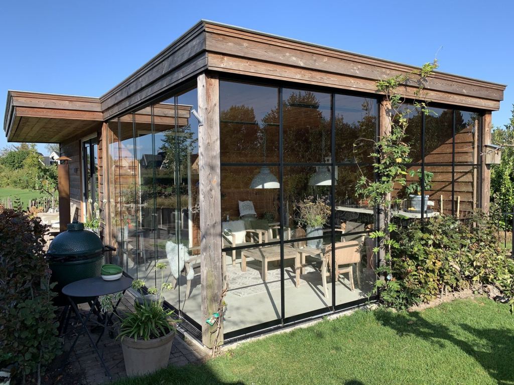 Moderne &Uuml;berdachung aus Holz mit Glasschiebew&auml;nden, stimmungsvoll eingerichtet mit Gartenm&ouml;beln.