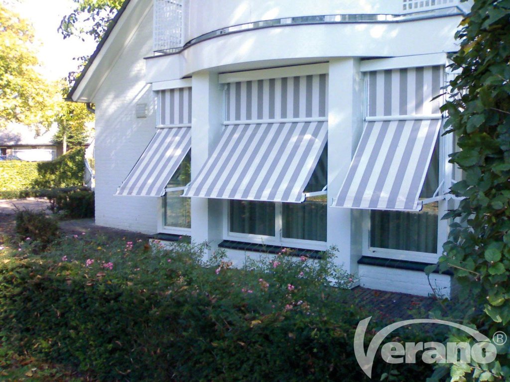 Strakke uitvalschermen wit grijs gestreept, gemonteerd aan een woning voor zonwering en privacy.