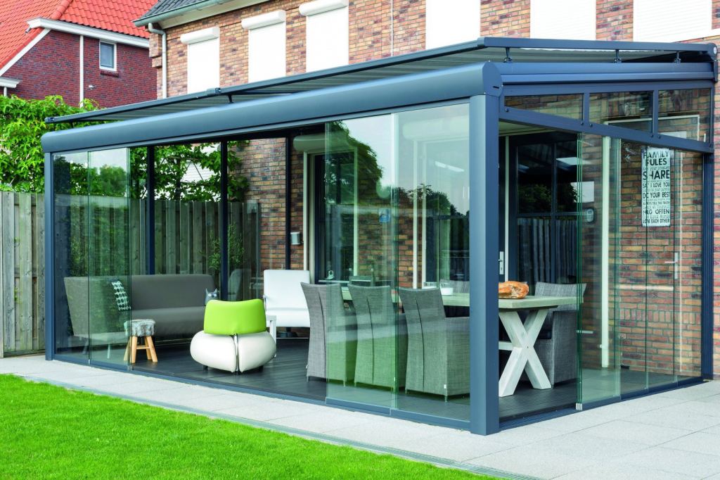 Modern veranda with glass walls, furnished with stylish furniture and green accents.